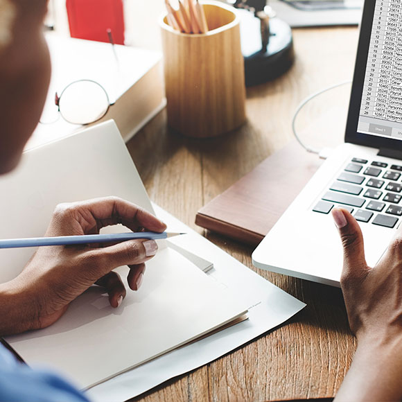 a person using a laptop with one hand while holding a pencil in the other hand