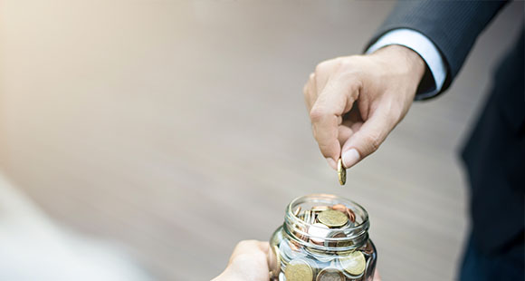 a business man placing a coin into a jar full of coins held by another person